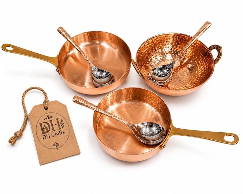 May include: Two copper pans with long brass handles, one round hammered copper bowl with side handles, and three silver-toned spoons. A rectangular brown paper tag with a jute string features the text DH DH Crafts and a small icon.