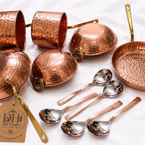 May include: A set of hammered copper kitchenware including two mugs, three bowls with brass handles, a frying pan with a long brass handle, and four spoons with copper-toned handles and silver-colored bowls. A brown tag displays the text DH Crafts.