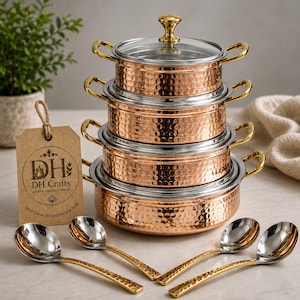 Peut inclure: Une pile de quatre casseroles en cuivre martelé avec des bords argentés et des poignées dorées, surmontée d'un couvercle en verre. Quatre cuillères argentées à manche doré sont disposées devant. Une étiquette en papier affiche DH Crafts.