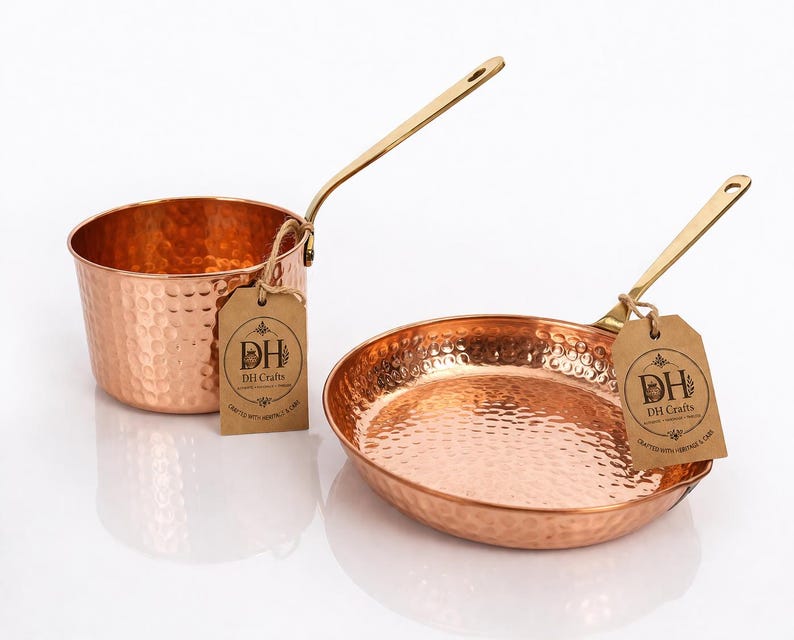 May include: A hammered copper saucepan and a matching frying pan, both featuring long brass-toned handles. Each piece has a brown paper tag attached with twine, printed with the text DH Crafts, Crafted with Heritage & Care.
