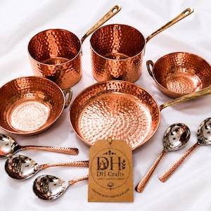 May include: A set of hammered copper cookware including two saucepans with long handles, two bowls with side handles, one frying pan, and four spoons with metallic bowls. A brown rectangular tag features the text DH Crafts and DH logo.