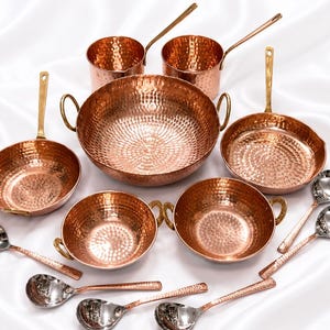 May include: A set of hammered copper cookware including a large central bowl with two handles, two smaller bowls with handles, two saucepans with long handles, and several silver-toned spoons. A brown paper tag displays the text DH Crafts.