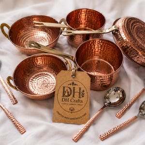 May include: A set of hammered copper cookware including two bowls with side handles, two saucepans with long brass handles, and four spoons with silver-toned bowls and textured copper handles. A brown paper tag features the text DH DH Crafts.