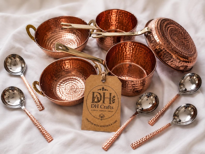 May include: A set of hammered copper cookware including two bowls with side handles, two saucepans with long brass handles, and four spoons with silver-toned bowls and textured copper handles. A brown paper tag features the text DH DH Crafts.