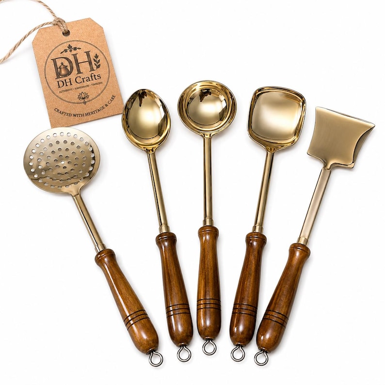 May include: A set of five gold-toned metal kitchen utensils with dark brown wooden handles, including a slotted spoon, a round spoon, a ladle, a square-edged spoon, and a flat turner. A brown paper tag with the text DH Crafts is attached.