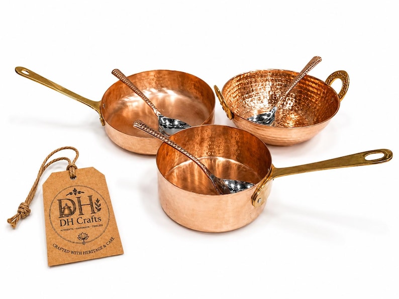 May include: A set of three copper cookware pieces including two pans with long brass handles and one bowl with two brass side handles. Each piece contains a silver-toned spoon. A brown paper tag features the text DH Crafts, Crafted with Heritage & Care.