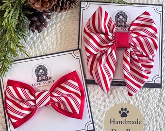 May include: Two fabric dog bows featuring a red and white candy cane striped pattern. Each bow is attached to a white display card with the Love, Scout The Doodle logo. The bows have a layered design with solid red fabric edges.