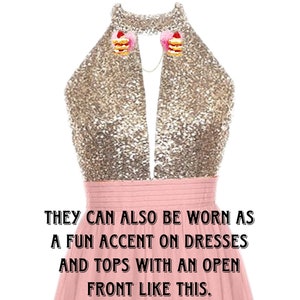 May include: A pink dress with a gold sequined top. The dress has a deep V-neckline and is styled with two small cake-shaped clips on the neckline. The text "EXAMPLE OF HOW TO WEAR CLIPS." is at the top of the image. The text "THEY CAN ALSO BE WORN AS A FUN ACCENT ON DRESSES AND TOPS WITH AN OPEN FRONT LIKE THIS." is at the bottom of the image.