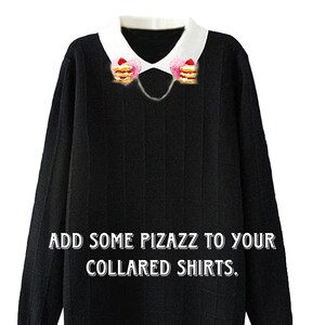 May include: A black sweater with a white collar and a chain with two strawberry and cream pancake charms attached to the collar. The text "EXAMPLE OF HOW TO WEAR CLIPS." is at the top of the image. The text "ADD SOME PIZAZZ TO YOUR COLLARED SHIRTS." is at the bottom of the image.