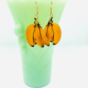 May include: A pair of gold dangle earrings with a cluster of yellow banana charms.