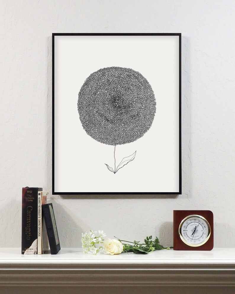 May include: Black and white floral art print in a black frame. The artwork features a detailed, circular flower head with a thin stem and leaf. A white mantel displays books, a small frame, flowers, and a wooden clock.