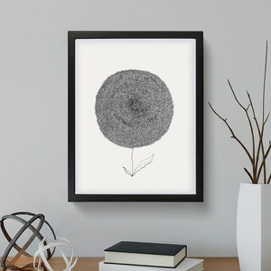 May include: Black framed art print featuring a detailed, grayscale illustration of a dandelion-like flower. The artwork is mounted on a white background. The image is displayed on a wooden surface with decorative objects.