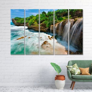 Op de afbeelding: Een meerpaneels canvasprint met een waterval die in de oceaan stroomt. Weelderig groen gebladerte en rotsachtige kliffen omlijsten de scène en creëren een rustig en schilderachtig landschap.
