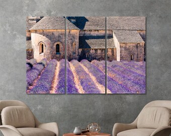 May include: A three-panel canvas print depicting a stone building with a lavender field in the foreground. The building has a weathered stone exterior and a tiled roof. The lavender field is in full bloom, with rows of purple flowers.
