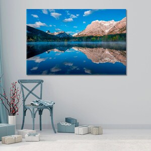 Pode incluir: Uma fotografia de paisagem que apresenta uma cordilheira refletida num lago tranquilo. As montanhas são cobertas de neve e o céu é azul com nuvens brancas. O lago é de um azul profundo e a água está calma e refletindo.