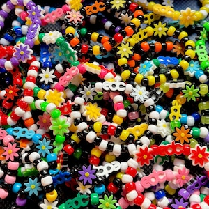 May include: A collection of colorful beaded bracelets with flower and EDC designs. The bracelets feature a variety of colors, including red, yellow, green, blue, and purple, with black and white beads. The bracelets are made of plastic beads.