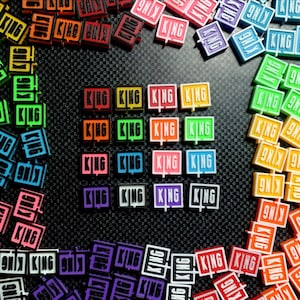 May include: A collection of colorful square tiles with the word "KING" printed on them. The tiles are arranged in a circle with a variety of colors, including red, orange, yellow, green, blue, purple, and pink.