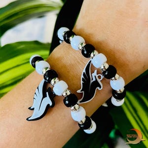 May include: Two black and white beaded bracelets with silver accents. Each bracelet has a charm attached, one is a black angel wing and the other is a white angel wing.