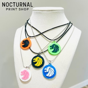 May include: Five circular pendants featuring a stylized lion head profile, each in a different color combination: orange with black, green with dark green, dark green with yellow, white with pink, and blue with white. Each hangs on a cord.