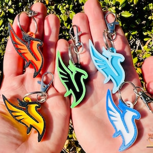 May include: Six colorful keychains featuring a stylized bird design. The keychains are made of plastic and come in a variety of colors, including orange, green, blue, yellow, and white.