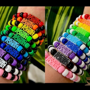 May include: A stack of colorful beaded bracelets with the words "Electric Forest" on each charm. The bracelets are arranged in a rainbow pattern, with red, orange, yellow, green, blue, indigo, and violet.