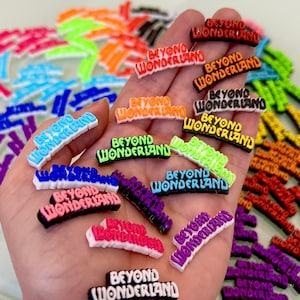 May include: A hand holding a variety of colorful plastic charms with the text "Beyond Wonderland" in different colors and fonts.