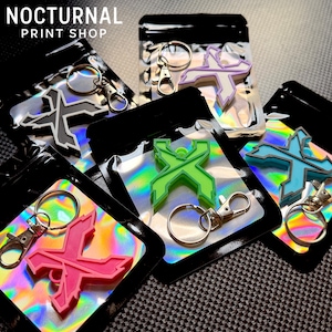 May include: Five individual keychains, each featuring a stylized letter X design in different colors including pink, lime green, light blue, lavender, and grey, packaged in clear plastic pouches with holographic backing and silver metal rings.