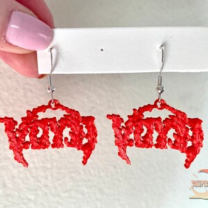 May include: A pair of red earrings with the word "VOID" written in a gothic font. The earrings are hanging from silver hooks.