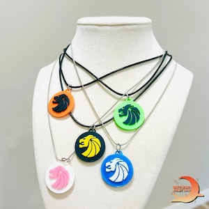 May include: A collection of colorful pendant necklaces displayed on a mannequin. Each necklace features a round pendant with a lion design in various colors, including orange, green, blue, black, and pink. The pendants are attached to either black cord or silver chains.