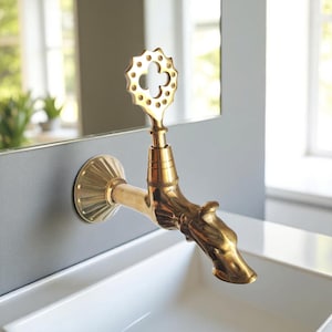May include: A gold-colored faucet with a decorative handle and a dragon-head spout. The faucet is mounted on a gray wall above a white sink. The handle has a clover-like design.