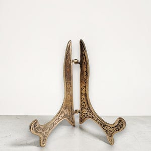 Pode incluir: Um suporte de moldura de latão em estilo vintage. O suporte tem um design ornamentado e texturizado e uma parte traseira articulada para estabilidade. O suporte tem aproximadamente 15 cm de altura.