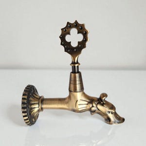 May include: Antique brass-colored faucet with a decorative dragon head spout and a floral-shaped handle. The faucet has a detailed, ornate design and is likely for decorative purposes.