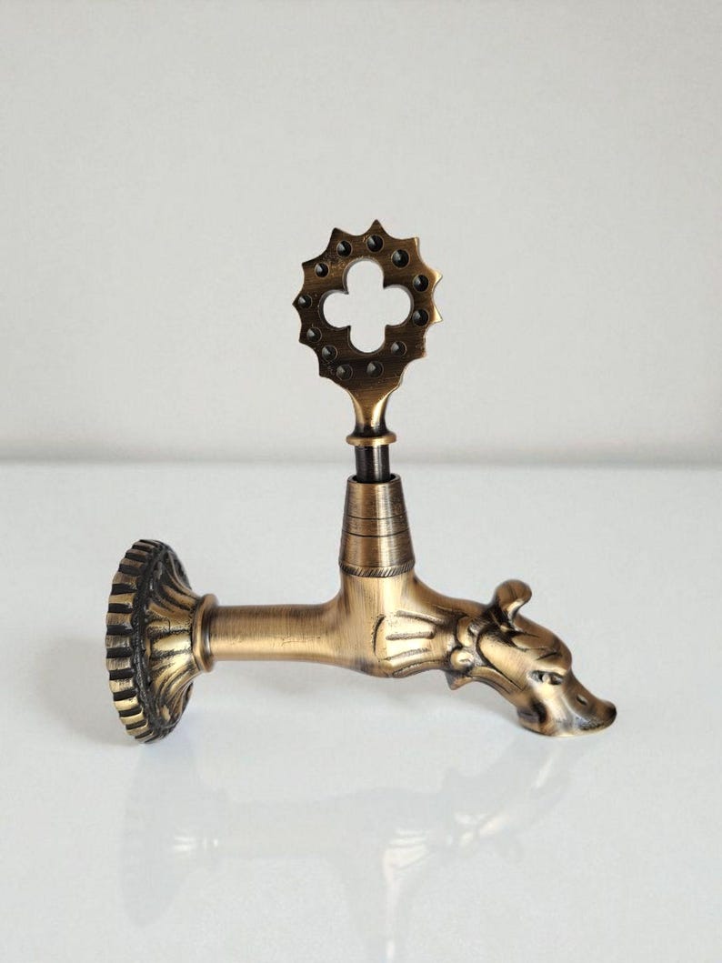 May include: Antique brass-colored faucet with a decorative dragon head spout and a floral-shaped handle. The faucet has a detailed, ornate design and is likely for decorative purposes.