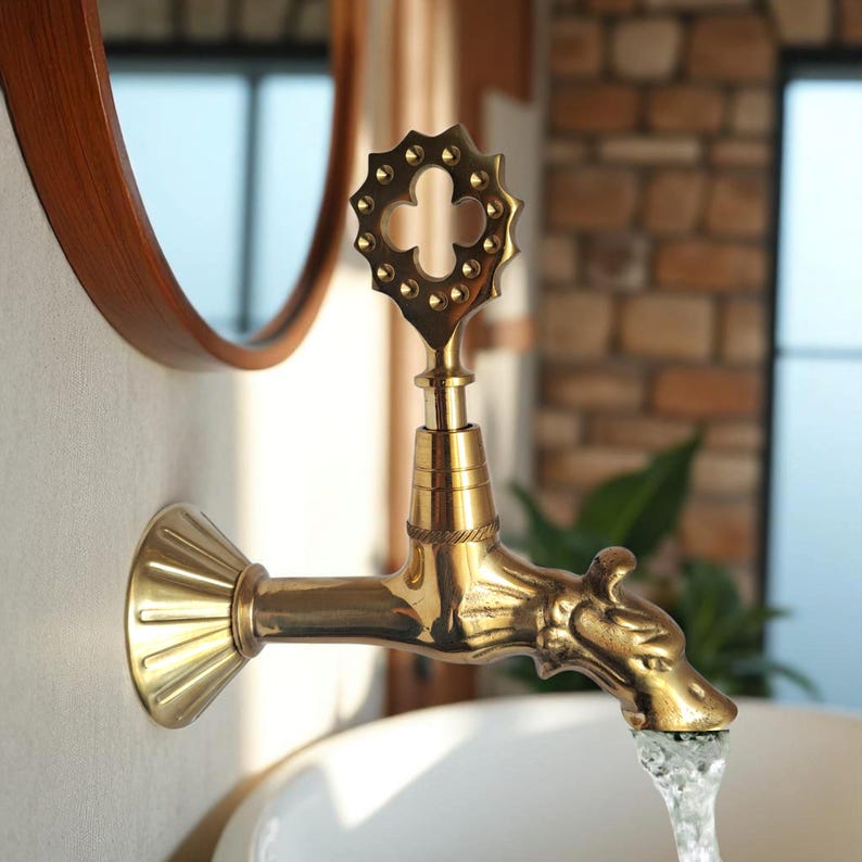 May include: A gold-colored faucet with a decorative cross-shaped handle and a dragon-head spout. The faucet is mounted on a white wall, with water flowing into a white basin. The design is vintage and ornate.