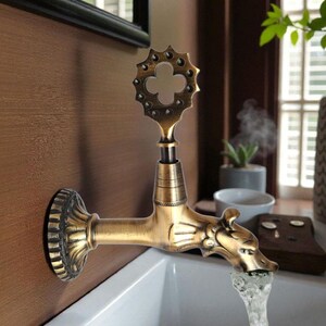 May include: An antique-style faucet with a decorative handle and a dragon-shaped spout. The faucet is made of brass and is mounted on a brown wall. Water flows from the spout into a white sink.