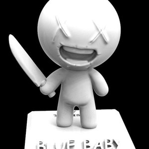 Può includere: Figurina bianca di un personaggio sorridente con X per gli occhi che tiene un coltello. La figurina è in piedi su una base con le parole "BLUE BABY" stampate su di essa.