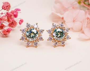 May include: A pair of gold earrings featuring a green gemstone centre surrounded by a halo of smaller white gemstones. The earrings are shaped like a star.