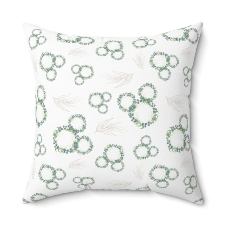 May include: White throw pillow with a repeating pattern of green leafy wreaths in the shape of Mickey Mouse's head.