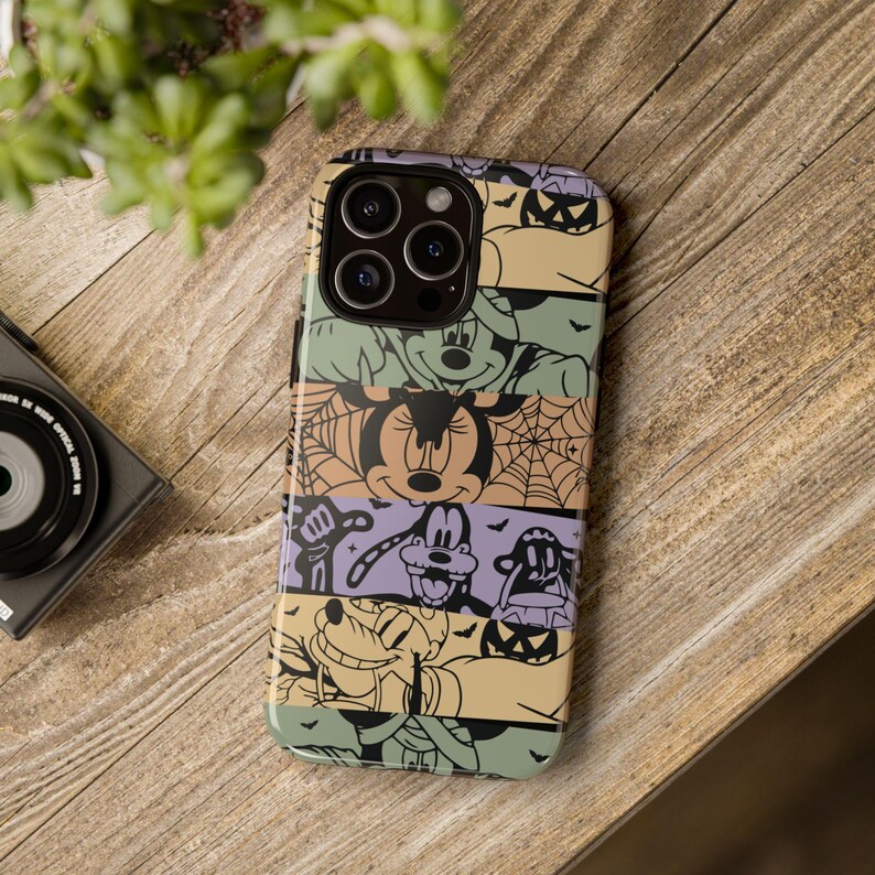 May include: A colorful phone case with a Halloween theme featuring Mickey Mouse, Minnie Mouse, Goofy, and Pluto. The case has a multi-colored background with black spiderwebs and bats.