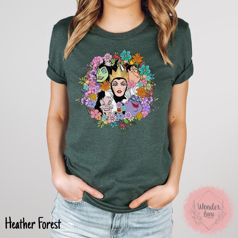 May include: A green t-shirt with a floral design featuring the faces of Disney villains, including Maleficent, Cruella de Vil, Ursula, and the Evil Queen. The design is surrounded by colorful flowers.