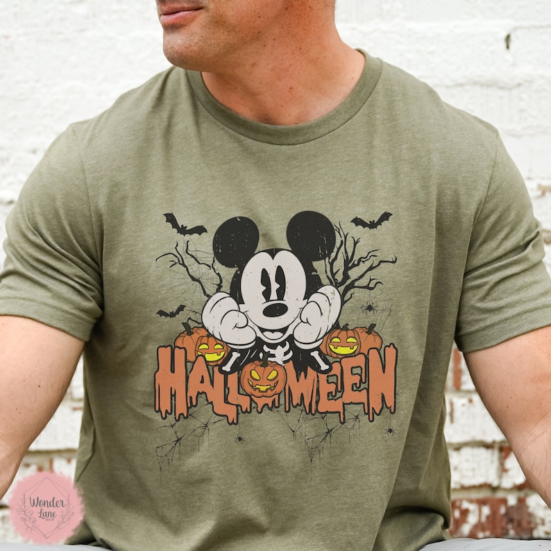 May include: A green t-shirt with a vintage-style graphic of Mickey Mouse dressed as a skeleton with pumpkins and bats. The text "HALLOWEEN" is dripping down the front of the shirt.