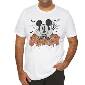 May include: White t-shirt with a vintage-style graphic of Mickey Mouse wearing a skeleton costume and surrounded by jack-o'-lanterns. The text "HALLOWEEN" is written in a dripping font below Mickey.