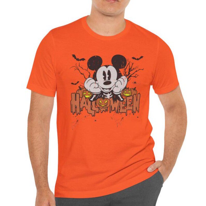 May include: Orange t-shirt with a cartoon image of Mickey Mouse dressed as a skeleton holding pumpkins. The text "HALLOWEEN" is printed below Mickey Mouse.
