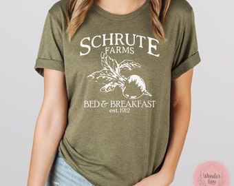 Puede incluir: Una camiseta verde con un diseño gráfico blanco que dice "Schrute Farms Bed & Breakfast est. 1912" con una ilustración de remolacha blanca.