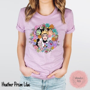 May include: A heather prism lilac t-shirt with a floral wreath design featuring the faces of Disney villains, including Maleficent, Cruella de Vil, Ursula, and the Evil Queen.