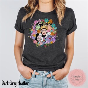 May include: Dark grey heather t-shirt with a floral wreath design featuring the faces of Disney villains: Maleficent, Ursula, Cruella de Vil, and the Evil Queen.