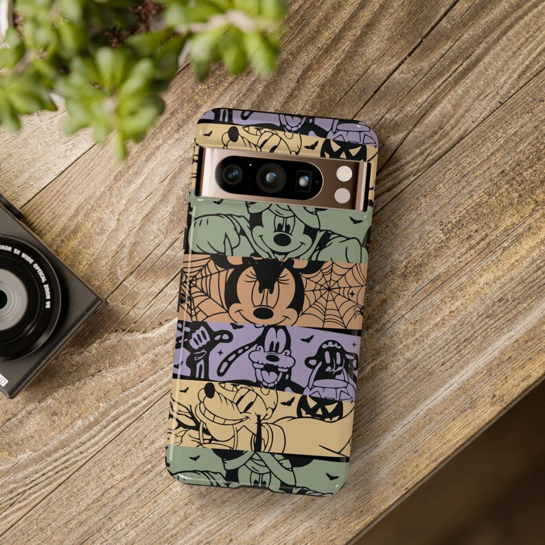 May include: A multi-colored phone case with a Halloween theme. The case features Mickey Mouse, Minnie Mouse, Goofy, and Pluto dressed in Halloween costumes. The case has a black and white striped background with a spiderweb pattern.