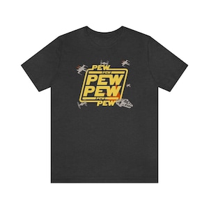 May include: A dark heather grey t-shirt with a yellow graphic of the words "PEW PEW PEW" in a box with a star wars inspired design.  The graphic is surrounded by small images of starfighters.