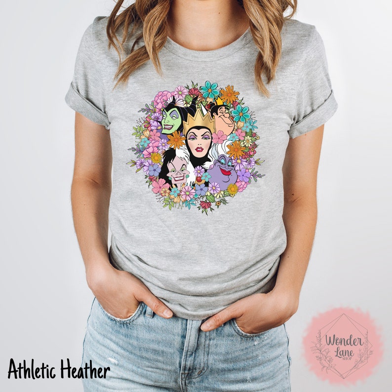 May include: A grey t-shirt with a floral wreath design featuring the faces of Disney villains, including Maleficent, Cruella de Vil, and Ursula. The text "Wonder Lane" is visible in the bottom right corner.