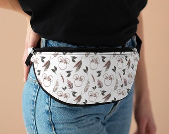 Puede incluir: Una riñonera blanca con una cremallera negra y un ribete negro. La riñonera tiene un estampado floral con detalles en rosa y marrón y una imagen repetida de orejas de Mickey Mouse.